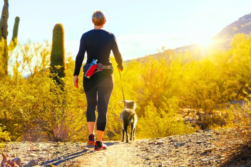A woman hiking in the desert with her dog.